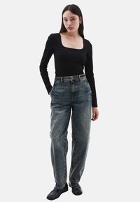 Top negro de manga larga con escote cuadrado, combinado con jeans de cintura alta de color azul claro. El modelo lleva unos zapatos negros gruesos.