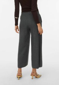 Pantalon large gris avec une taille côtelée, en matière douce. Associé à des sandales à talons jaunes avec un motif reptile.