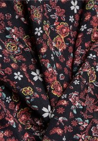 Tissu noir avec un motif floral dense de fleurs rouges, jaunes, blanches et bleues, présenté en gros plan les plis et la texture.