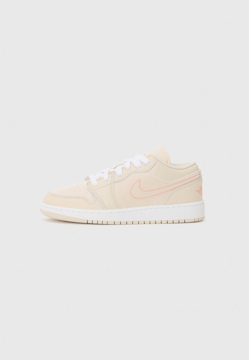 Baskets basses beige avec lacets blancs, swoosh Nike rose et semelle blanche sur un fond clair uni.