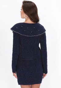 Vestido de punto azul marino con un patrón de trenzas texturizado, cuello sobredimensionado adornado con perlas, diseño ajustado y mangas largas.