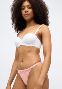Soutien-gorge blanc rembourré avec des bretelles réglables, associé à un string en dentelle rose orné de broderies florales et d'un accent doré à l'avant.