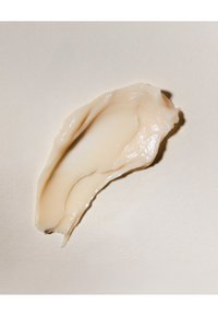 Crème ou lotion beige lisse avec une texture brillante sur un fond neutre clair.