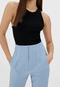 Svart ribbad tanktopp tillsammans med ljusblå högmidjade byxor. Byxorna har veck och sidfickor för extra detaljer.