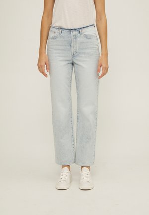 Helle blaue hochgeschnittene Jeans aus Denim, mit geradem Bein, leichtem Verblassen und klassischem Fünf-Taschen-Design. Dazu weiße Sneaker.