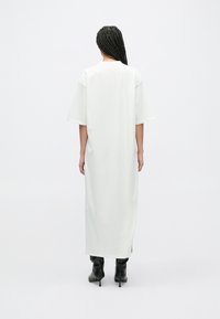 Lang, hvit t-skjortekjole med korte, vide ermer, sidesplitt og avslappet passform, kombinert med svarte støvletter med hæl. Jevn tekstur.