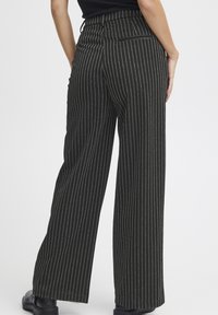 Široke hlače iz črne tkanine z diskretnim vertikalnim črtastim vzorcem, z visokim pasom in podrobnostjo na zadnjem žepu.