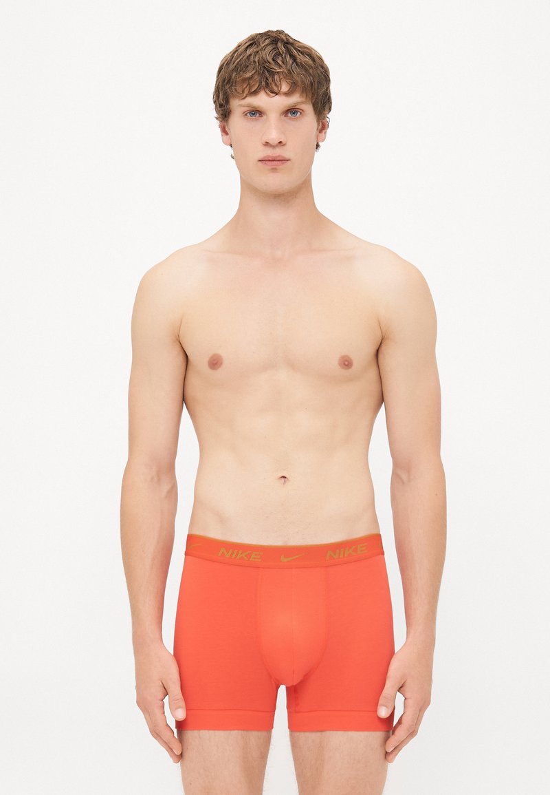 Red Nike boxer briefs with a fitted design. Elastic waistband features contrasting yellow lettering. Smooth cotton fabric.