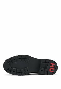 Semelle en caoutchouc noir avec des crampons profonds et le texte rouge "HU" sur le talon pour l'adhérence et le branding.