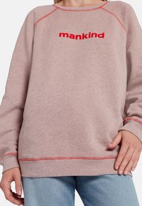 Sweatshirt rose avec des coutures rouges et "mankind" brodé en rouge. Il a une coupe décontractée et des manches longues. Texture de matériau douce.