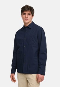 Mörkblå långärmad skjorta med knappar, tillverkad av slät tyg, med en bröstficka och svarta knappar, samt krage.