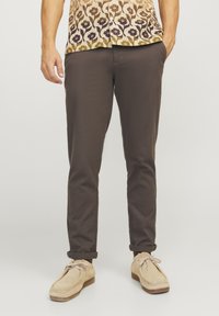 Ciemnobrązowe spodnie slim-fit z fakturowanej tkaniny, z wywiniętym dołem, w połączeniu z beżowymi zamszowymi butami i wzorzystą koszulą z krótkim rękawem.