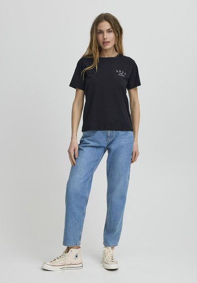 Tricou negru din bumbac cu mâneci scurte și guler rotund. Blugi din denim albastru deschis și adidași bej cu glezna înalță completează ținuta.