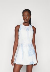 Bela športna obleka z jasno modrimi abstraktnimi vzorci, brezrokavni dizajn in okrogla ovratnika. Nike logotip na prsih, strukturirana tkanina.