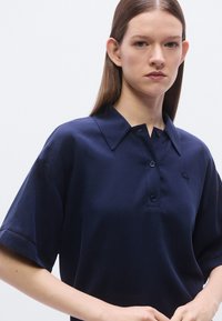 Polo bleu marine à manches courtes, avec un col et une patte à deux boutons ; présente une broderie de logo subtile sur la poitrine.
