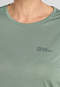 Helles grünes T-Shirt mit Rundhalsausschnitt, aus glattem Stoff gefertigt, mit einem Drucklogo in einer dunkleren Grüntönung auf der Brust.