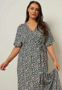 Svart och vit mönstrad omlottklänning med korta ärmar, v-ringning och justerbart knytbälte, med ett flödande, strukturerat tyg.