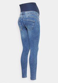 Jeans ajustados de maternidad con una cintura elástica de color azul oscuro, cuerpo de denim azul claro, diseño de cinco bolsillos y ajuste slim.
