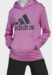Sweatshirt à capuche rose avec un grand logo Adidas noir, dotée d'une poche avant et de manches longues. Texture lisse et coupe athlétique.
