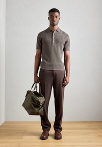 Polo de punto marrón de manga corta con cuello y tres botones, combinado con pantalones marrones oscuros y un bolso verde con acentos marrones.