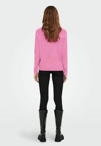 Pull rose décontracté avec des poignets et un ourlet côtelés, associé à un jeans skinny noir et des bottes noires jusqu'aux genoux.