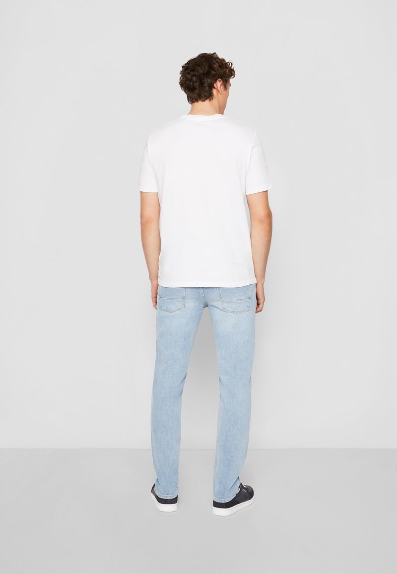 T-shirt bianco a maniche corte abbinato a jeans in denim azzurro chiaro e sneakers nere, caratterizzato da un design a gamba dritta e dettagli minimi.