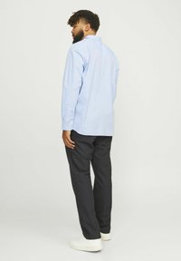  Lichtblauwe langslijfshirt met knopenmanchetten, gecombineerd met zwarte broek en witte sneakers. Gladde stof, slim fit en klassieke kraag.