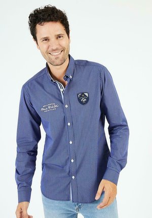 Chemise bleue marine à boutons pour homme avec un motif à micro carreaux, manches longues, un écusson sur la poitrine et un col intérieur à rayures contrastées.