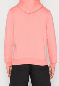Sudadera rosa con capucha ajustable, mangas largas y dobladillo acanalado. Confeccionada en un tejido suave, presenta una textura lisa y un diseño minimalista.