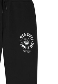 Zwarte sweatpants met een witte ronde grafiek van een schip en tekst "Lyle & Scott" en "Crafted for the Bold." Zachte katoenen stof.