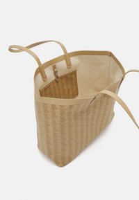 Sac fourre-tout beige avec un motif géométrique, des poignées en cuir et une poche intérieure contrastante. Présente une forme structurée et une texture lisse.