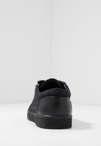 Černé tenisky s texturovaným prošívaným designem, hladkou černou patou a gumovou podešví. Obsahují zip na zadní straně pro snadné obouvání.