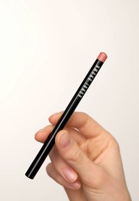 Lepenn i en blank svart forpakning med en rosa tupp, som har hvit tekst med merkevaren. Holdt mellom fingrene mot en nøytral bakgrunn.