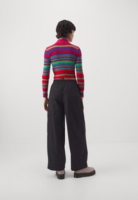 Pestrý pruhovaný zkrácený svetr s límečkem, doplněný volnými černými cargo kalhotami. Outfit dotváří černé platformové boty.