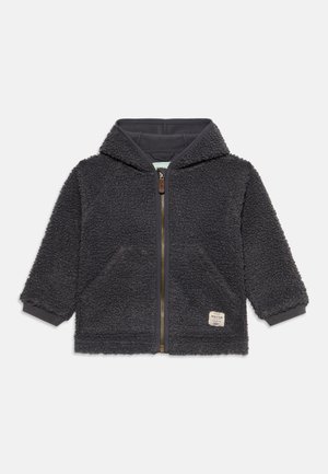 Donkergrijze fleece hoodie met rits, voorzakken, geribde boorden en een klein label aan de onderkant vooraan rechts.