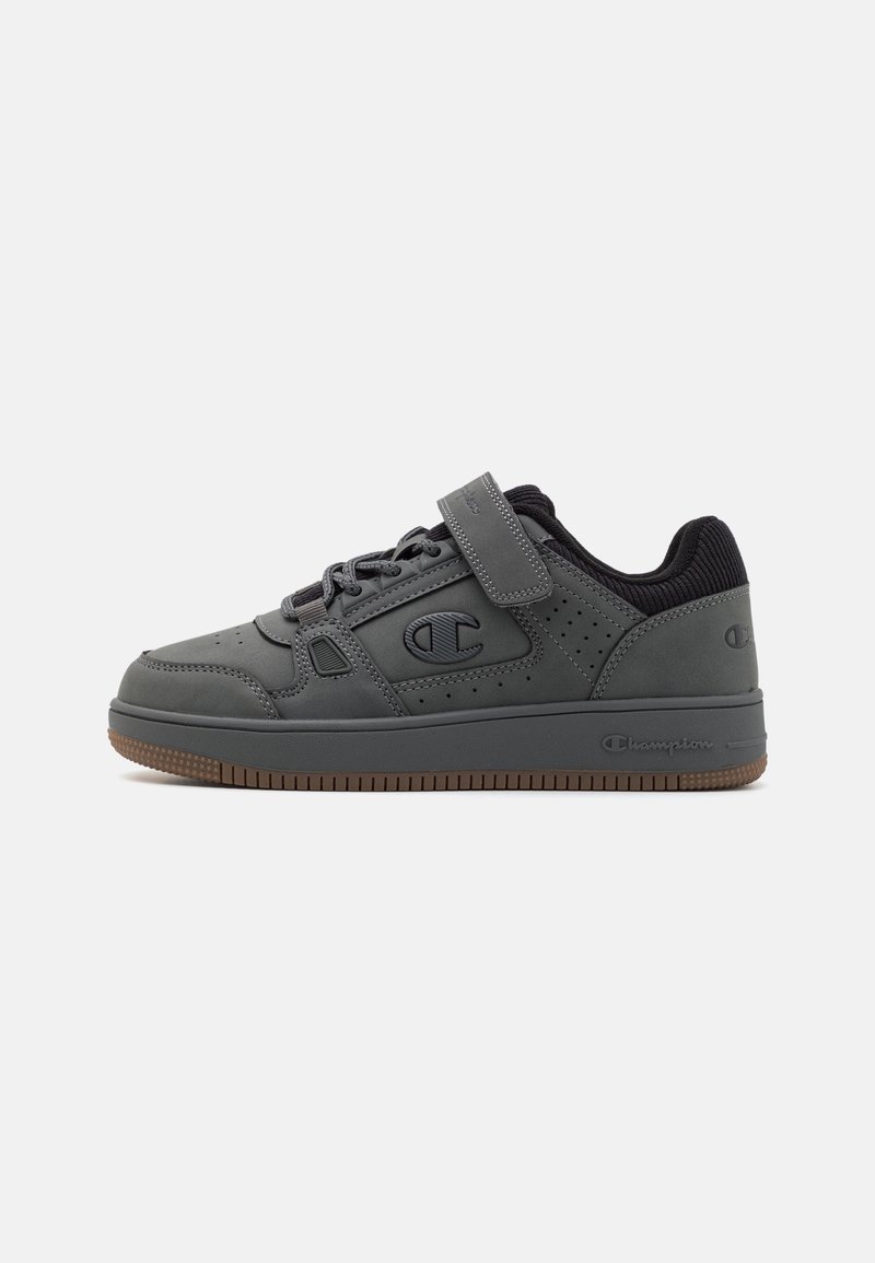 Zapatos deportivos grises con material similar al cuero, diseño perforado, collar acolchado, cierre de cordones y cinta de Velcro, y suela de goma.