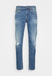 Jeans de denim azul con un lavado desvanecido y un desgarro desgastado en la rodilla izquierda, con bolsillos delanteros y trabillas para cinturón.