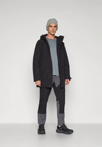 Black jacket with a hood, grey shirt, and black and grey pants. Styled with a grey beanie and black sneakers, featuring multiple pockets.