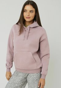 Haut à capuche violet clair avec des cordons, poche kangourou et poignets côtelés, associé à un pantalon gris à motif léopard. Texture de tissu douce.