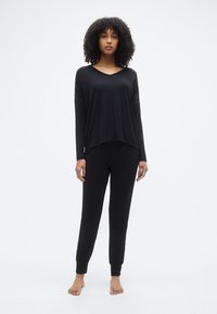 Σετ μαύρης ένδυσης lounge που αποτελείται από μπλούζα με μακριά μανίκια, V-λαιμόκοψη και δαντέλα στα μανίκια, σε συνδυασμό με εφαρμοστά μαύρα παντελόνια.