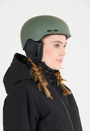 Matte oliven grøn skihjelm med ventilationsåbninger, sorte ør covers og en justerbar hakrem. Sammen med en sort jakke.