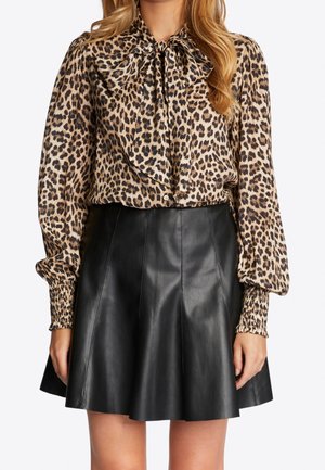 Kobieta ubrana w długorękawową bluzkę w panterkę z kokardą oraz czarną skórzaną spódnicę w kształcie litery A, pokazana od połowy uda do szyi.