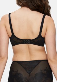 Sort blonde bh med justerbare stropper og en hægte- og øje-lukning på bagsiden. Har et blomsterdesign på en gennemsigtig bund.