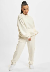 Cremefarvet loungewear sæt med en afslappet sweatshirt og matchende cargo bukser. Blødt materiale, oversized pasform og sidelommer.