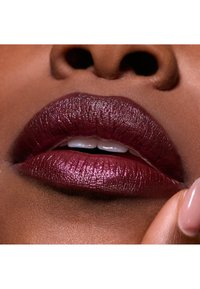 Rouge à lèvres bordeaux profond avec une texture glossy, mettant en valeur les contours lisses des lèvres, accentué par un léger scintillement et des contours bien définis.
