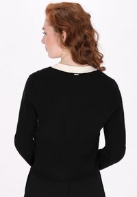 Pulover negru tricotat cu guler de culoare crem; are mâneci lungi și o siluetă ajustată; detaliu hardware vizibil pe spate.