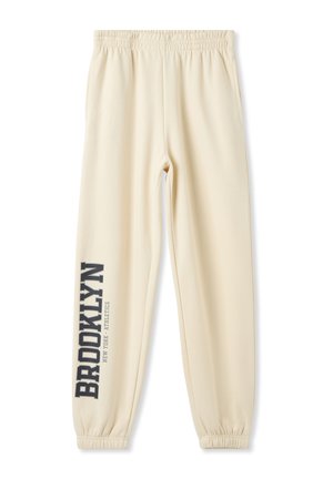 Pantaloni da jogging color crema con una vita elastica, gambe affusolate e la scritta "BROOKLYN" stampata in grigio scuro sul lato sinistro.