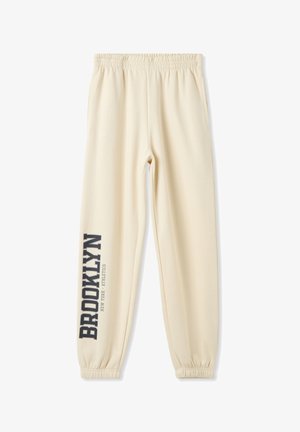 Pantaloni da jogging color crema con una vita elastica, gambe affusolate e la scritta "BROOKLYN" stampata in grigio scuro sul lato sinistro.