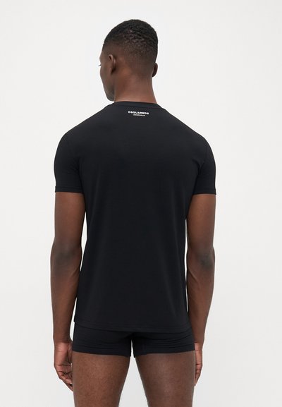 Ein Mann steht von hinten und trägt ein enges schwarzes T-Shirt mit dem weißen Text "DSQUARED2 UNDERWEAR" auf dem oberen Rücken sowie schwarze Boxershorts.