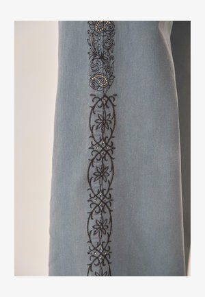 Tela azul claro con bordado floral y de paisley negro adornado con pequeñas tachuelas metálicas en un patrón vertical.